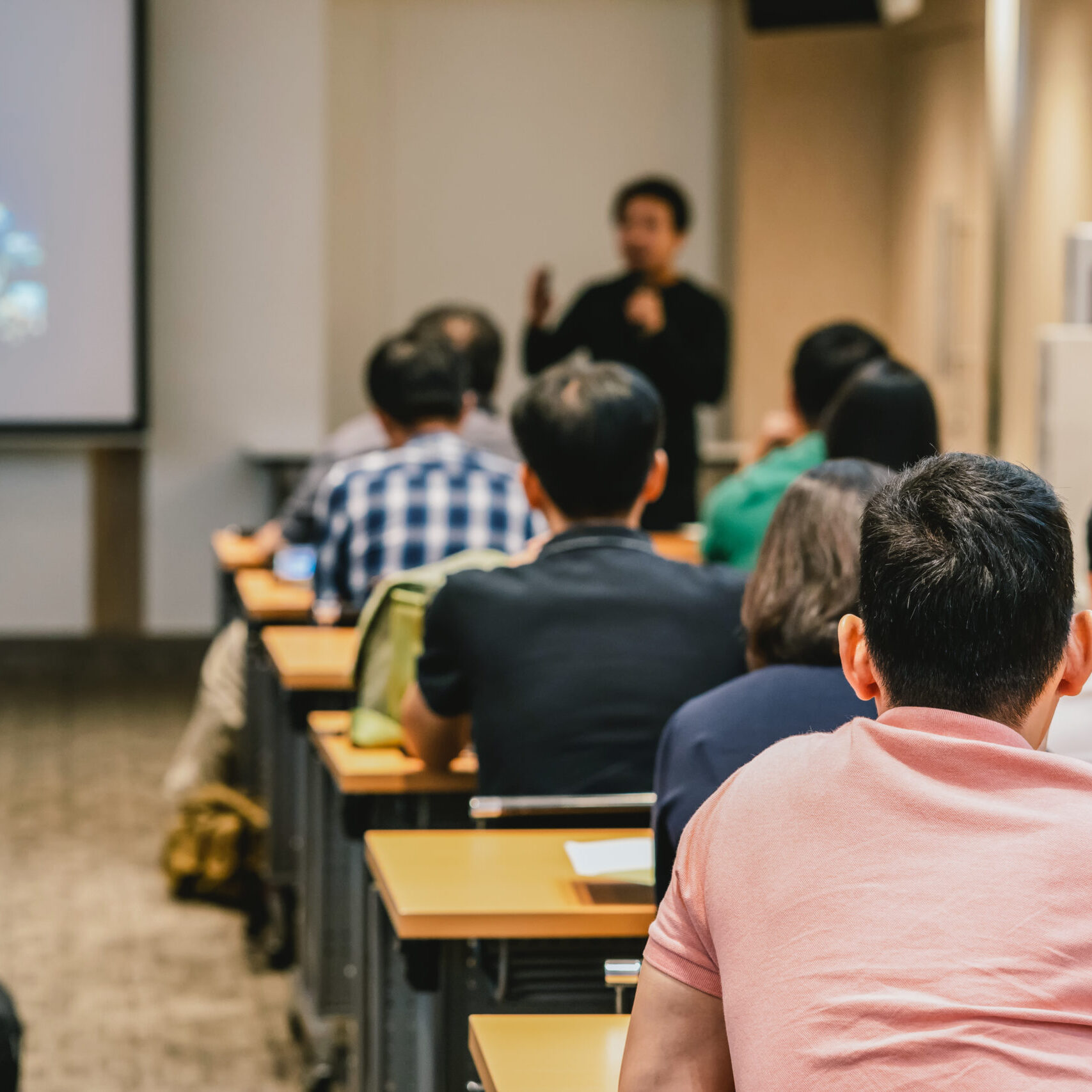 Speaker on the stage in front of the room with Rear view of Audience in put hand up acton for answer the question in the meeting or seminar meeting, business and education concept